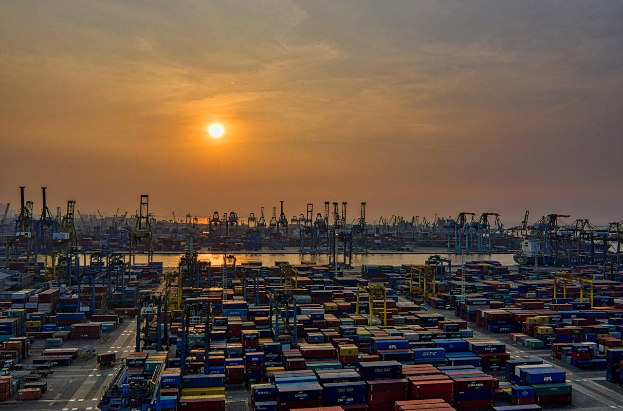 The Art of Drawing Readers In: Your attractive post title goes here Sunset over a bustling seaport filled with stacked shipping containers and cranes.