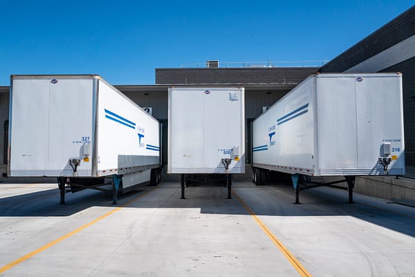 About Three white cargo trailers parked at an industrial shipping dock under clear blue skies.